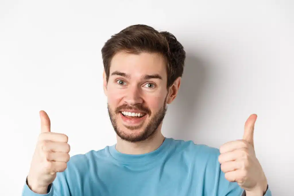 close up of cheerful man say yes showing thumbs up in approval praise good job smiling approvingly standing on white background