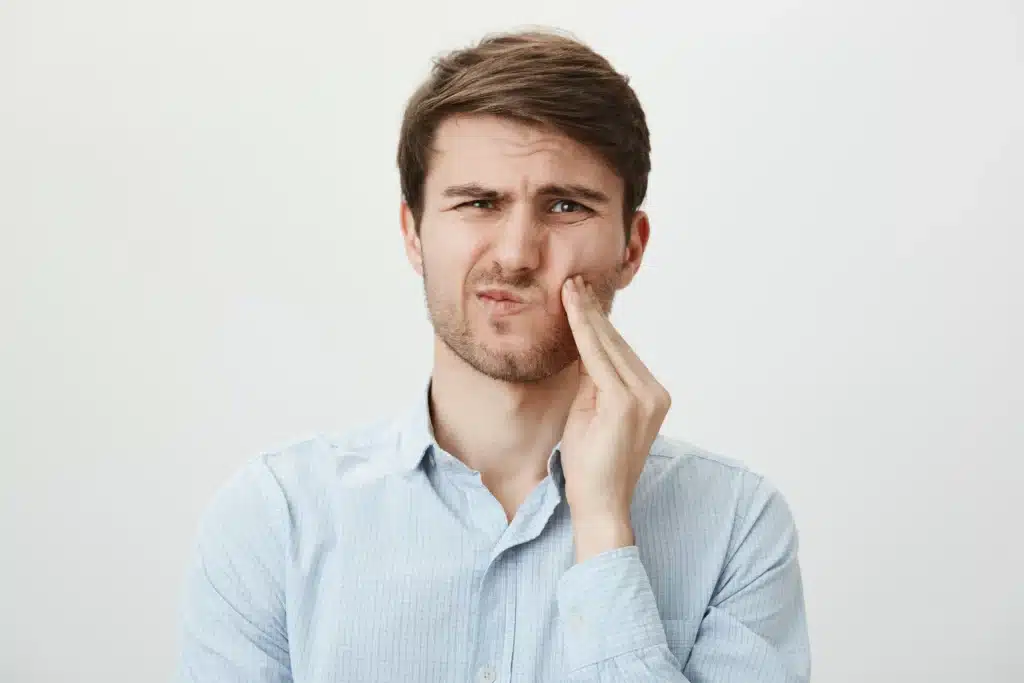 man touching cheek and grimacing from pain from toothache need dentist