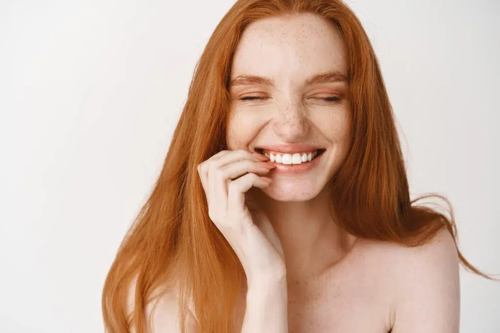 close up happy redhead woman with pale no makeup skin perfect smile laughing looking joyful standing naked white wall